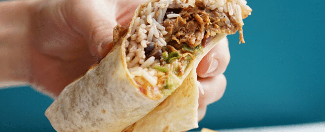 Benito's Burrito being held by a person, close up of all the delicious fillings inside