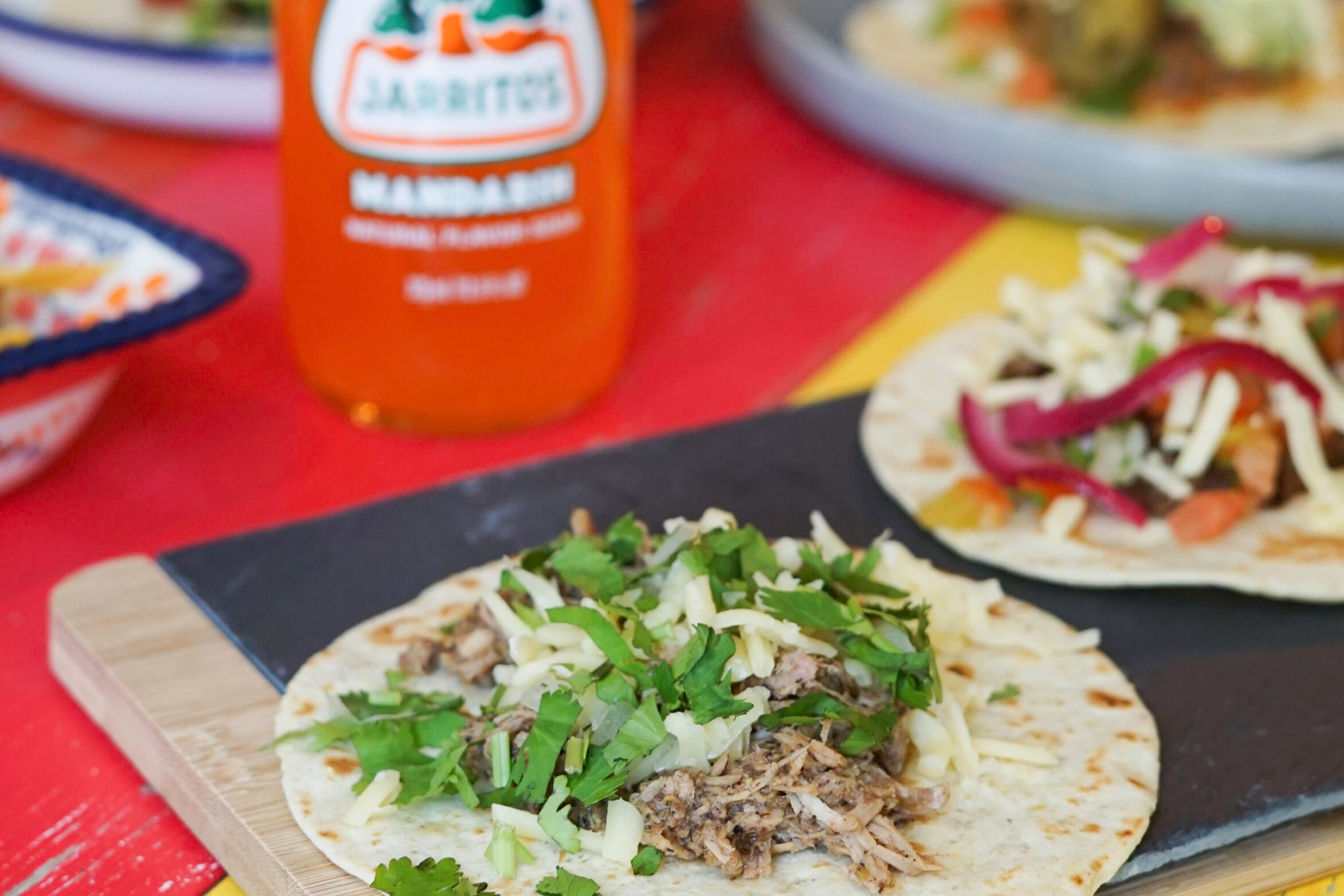 Three tacos on a cutting board next to a bottle of salsa, ready to be enjoyed.