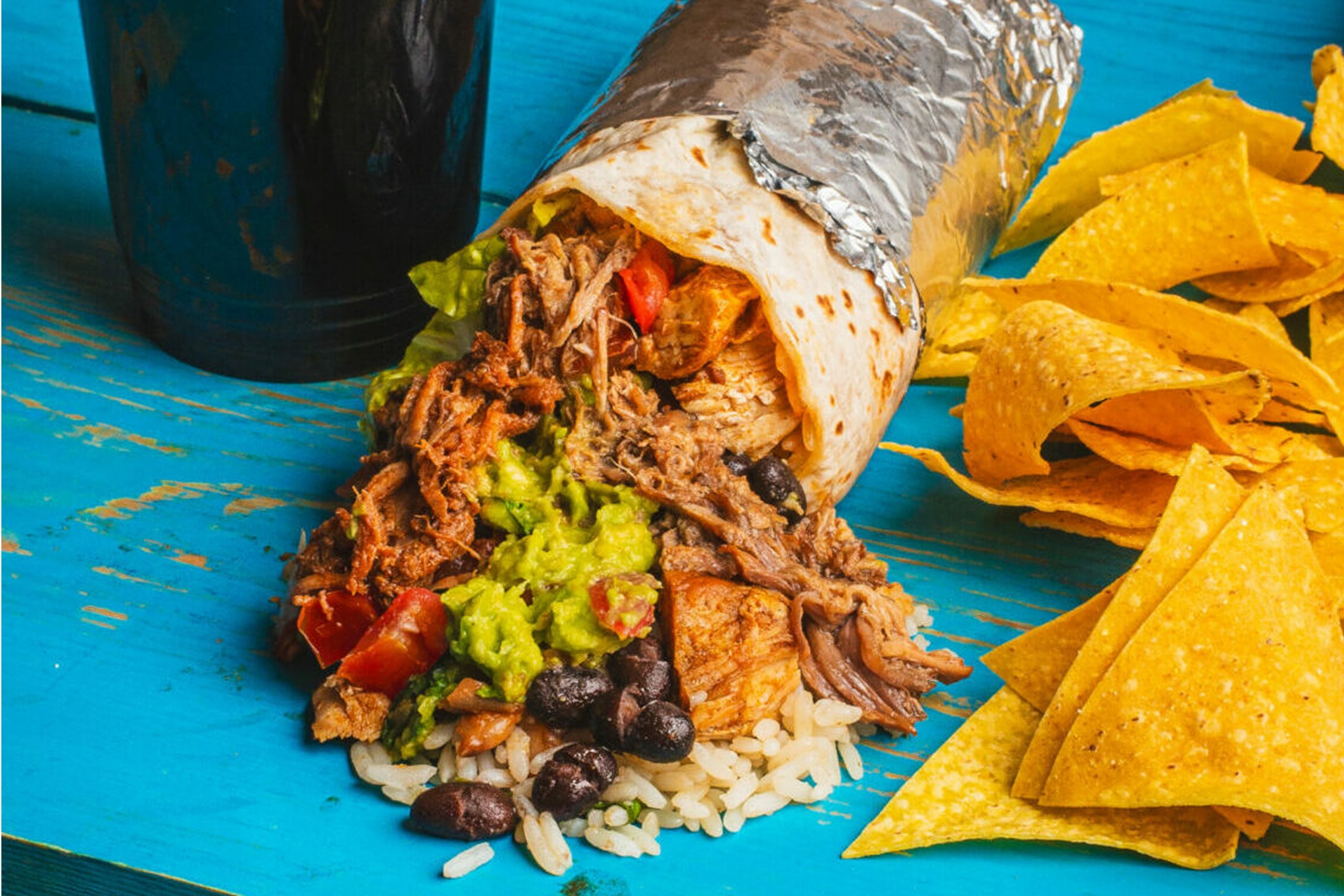 Burrito filled with rice, beans, avocado, guacamole, served with tortilla chips and salsa on the side.