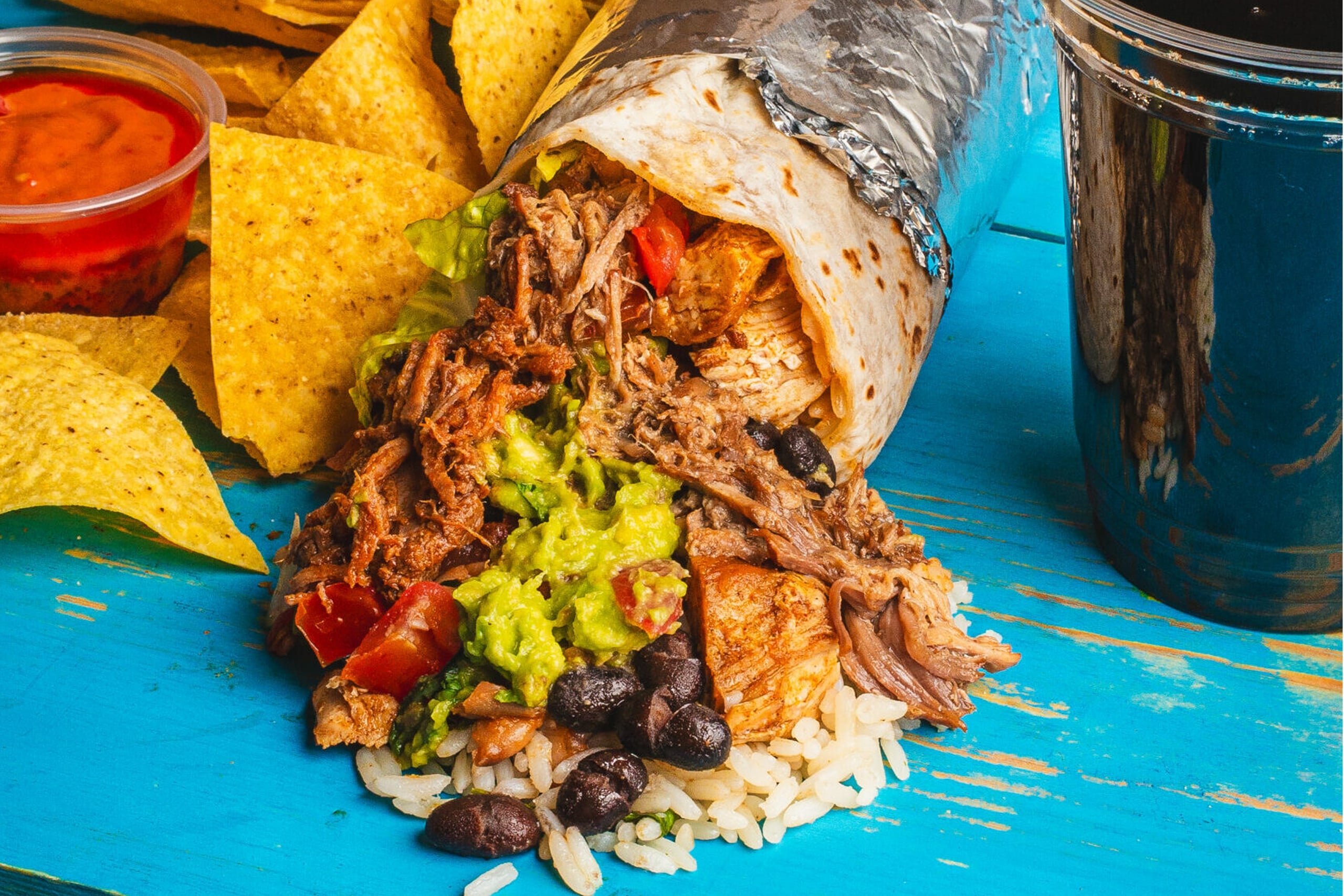 Burrito filled with rice, beans, avocado, guacamole, served with tortilla chips and salsa on the side.