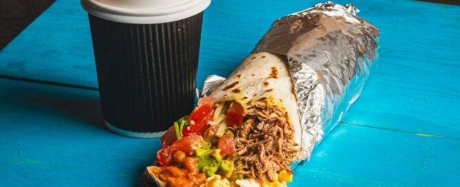 A burrito and a steaming cup of coffee sit on a wooden table, ready for a delicious meal.