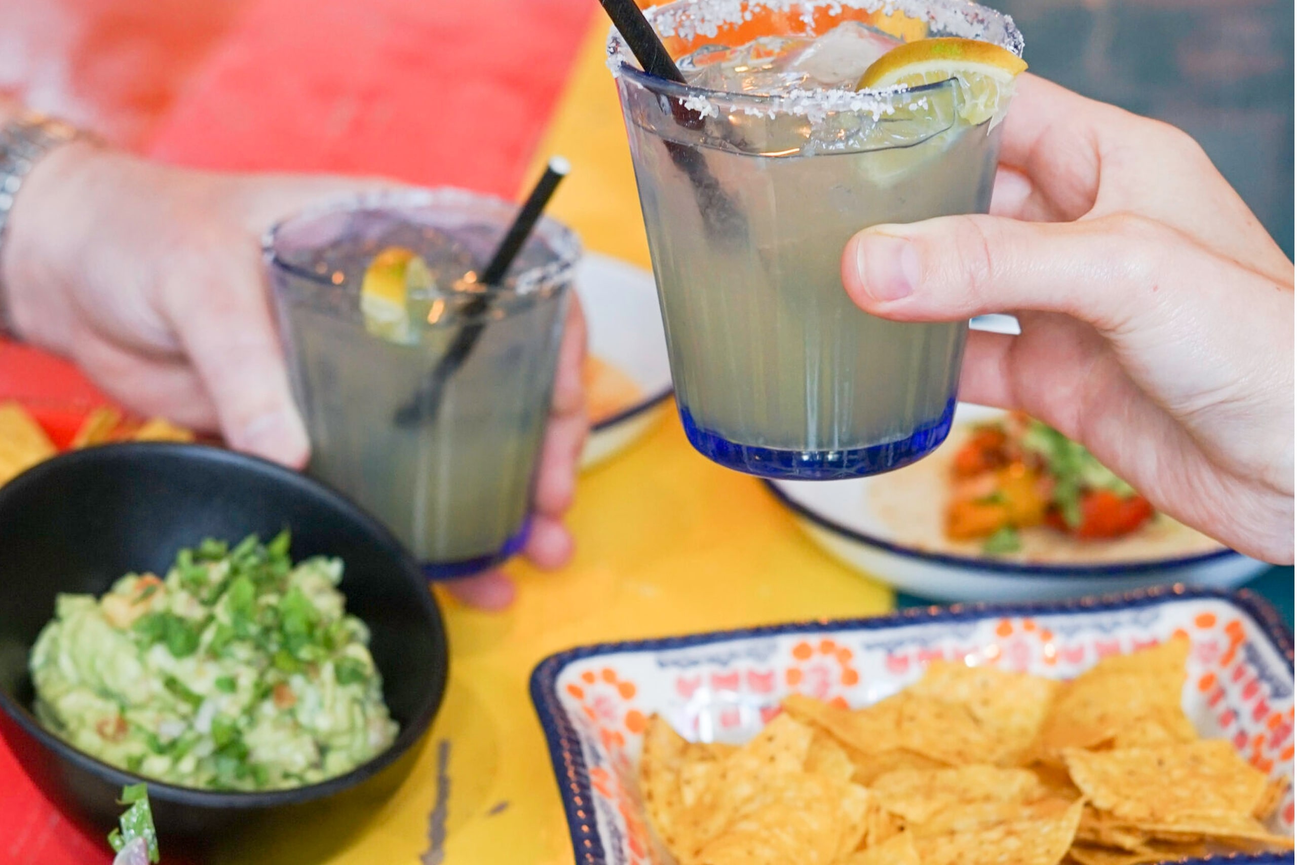 Two people enjoying drinks and chips together at a table, smiling and chatting.