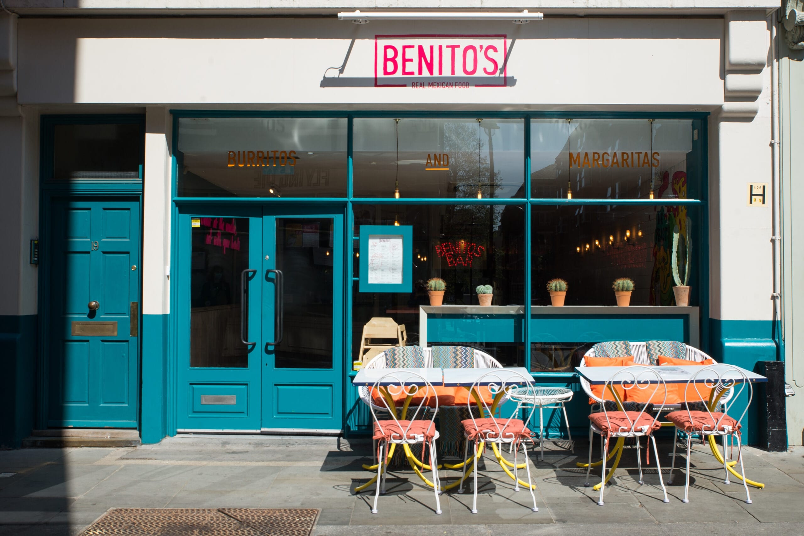 Outdoor dining area of a restaurant featuring several tables and chairs under a clear blue sky.